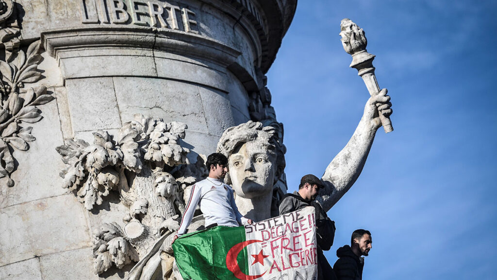 The Algerian flag with the words written on it that read, 'System get out, free Algeria' is held as protesters rally against the Algerian president's bid for a fifth term in office on February 24, 2019 at the Place de la Republique in Paris. - President Abdelaziz Bouteflika is Algeria's longest-serving president and a veteran of its independence struggle who has clung to power since 1999 despite his ill health. (Photo by STEPHANE DE SAKUTIN / AFP)        (Photo credit should read STEPHANE DE SAKUTIN/AFP/Getty Images)