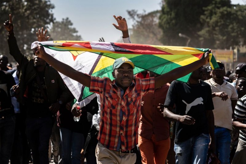 A man holding Zimbabwe's national flag walks with other protesters as they march in the streets of Harare on August 16, 2019. - Riot police in Zimbabwe fire teargas and beat demonstrators on August 16 during a crackdown on opposition supporters who have taken to Harare's streets despite a protest ban. Scores of people gathered in the capital's Africa Unity Square to demonstrate against the country's worsening economy in defiance of the ban, which was upheld by a court on August 16. (Photo by Zinyange Auntony / AFP)        (Photo credit should read ZINYANGE AUNTONY/AFP/Getty Images)